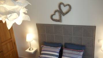 A bedroom with a bed, two heart-shaped wall decorations, a nightstand with a lamp, and a wooden wardrobe.