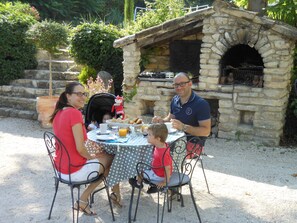 A family dining outdoors at a stone-built outdoor kitchen area with a table set for four. - Bastide De La Lézardière (Fontaine-de-Vaucluse)