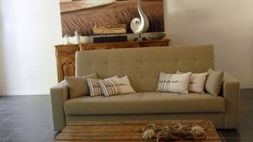 Una sala de estar con un sofá color beige, almohadas a rayas, una mesa de centro de madera y un cuadro grande de un paisaje marino.