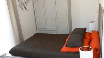 A bedroom with a bed, a nightstand, a lamp, a wardrobe, and a decorative wall piece.