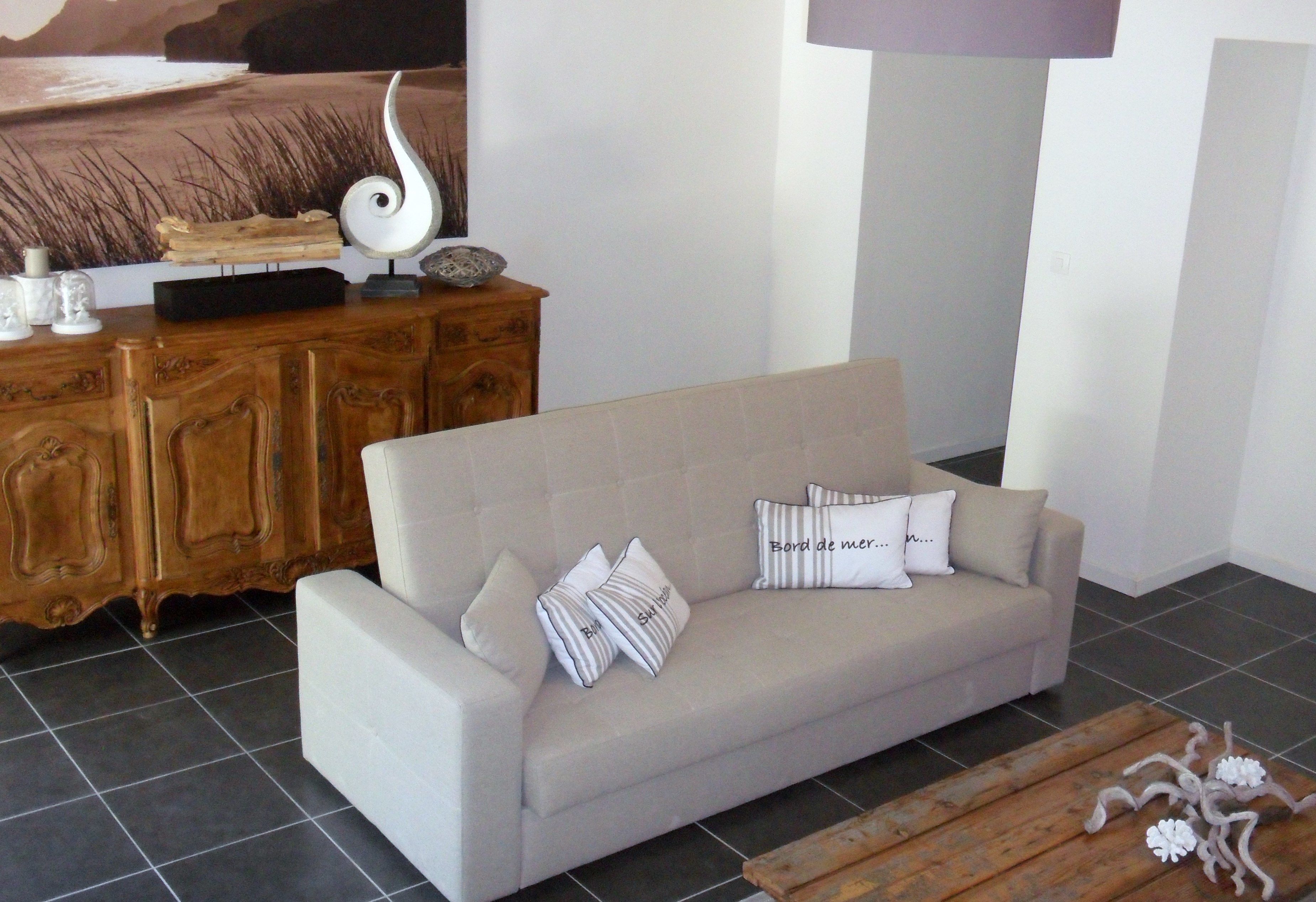 Ein Wohnzimmer mit einem beigefarbenen Sofa, Zierkissen, einem Holzschrank und einer modernen Lampe.