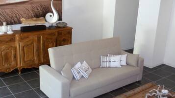 Ein Wohnzimmer mit einem beigefarbenen Sofa, Zierkissen, einem Holzschrank und einer modernen Lampe.