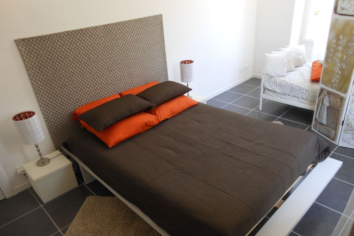 Ein modernes Schlafzimmer mit einem großen Bett, einem strukturierten Kopfteil und einem kleinen Nachttisch mit Lampe.