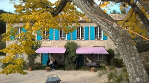 A stone building with blue shutters, a covered porch, and outdoor seating. - Bastide De La Lézardière (Fontaine-de-Vaucluse)