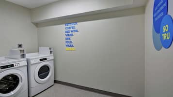 A laundry room with two front-loading washing machines, a wall-mounted dryer, and a motivational poster.