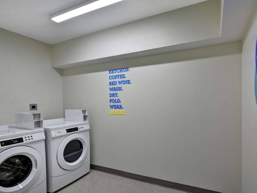 A laundry room with two front-loading washing machines, a wall-mounted dryer, and a motivational poster.