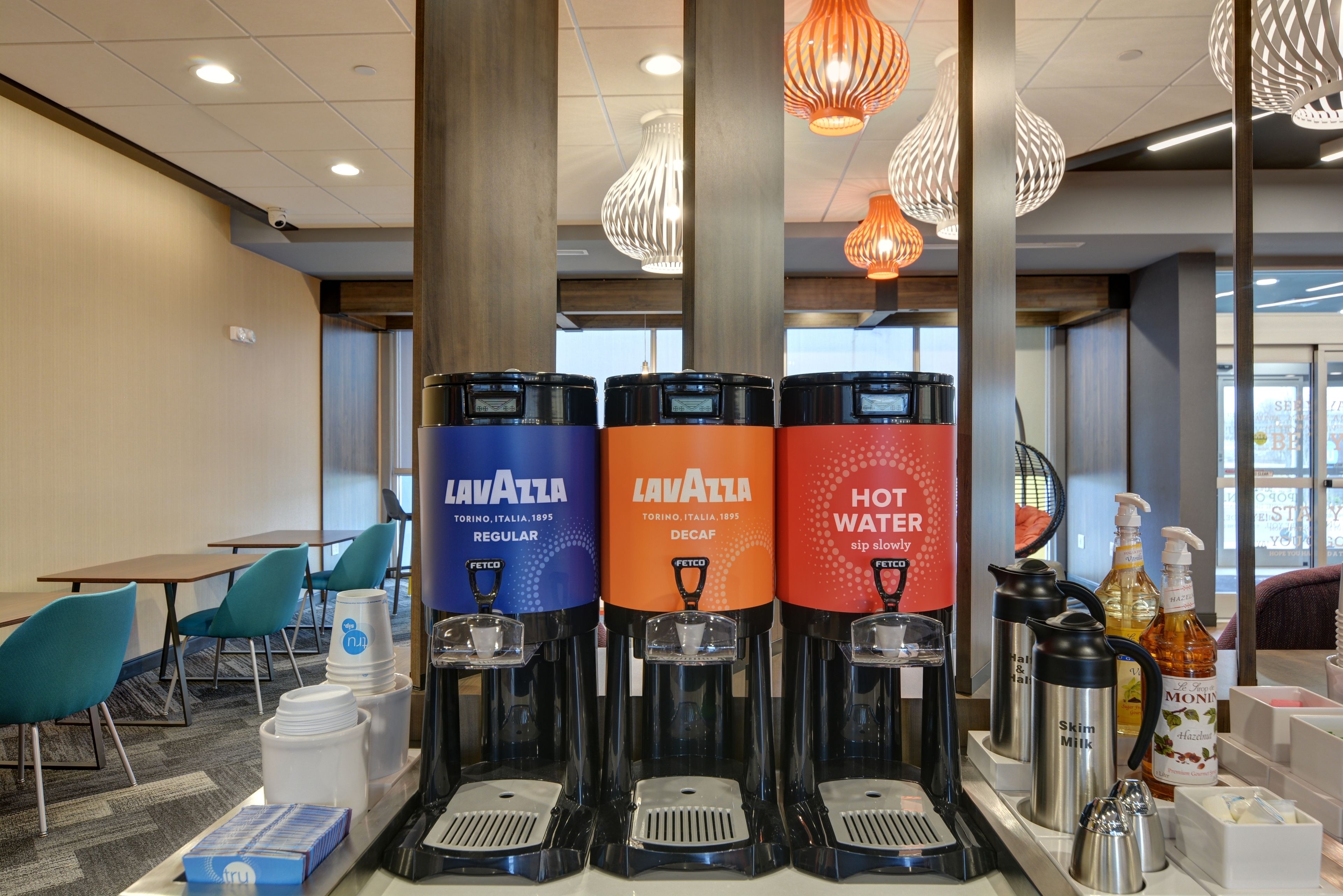 A hotel lobby with three beverage dispensers labeled 'Lavazza' and 'Hot Water'.