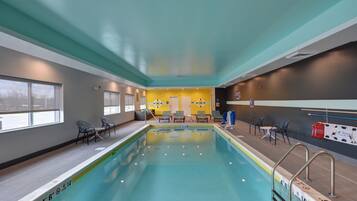 An indoor swimming pool with clear lane markings, a changing room area, and seating by the pool.