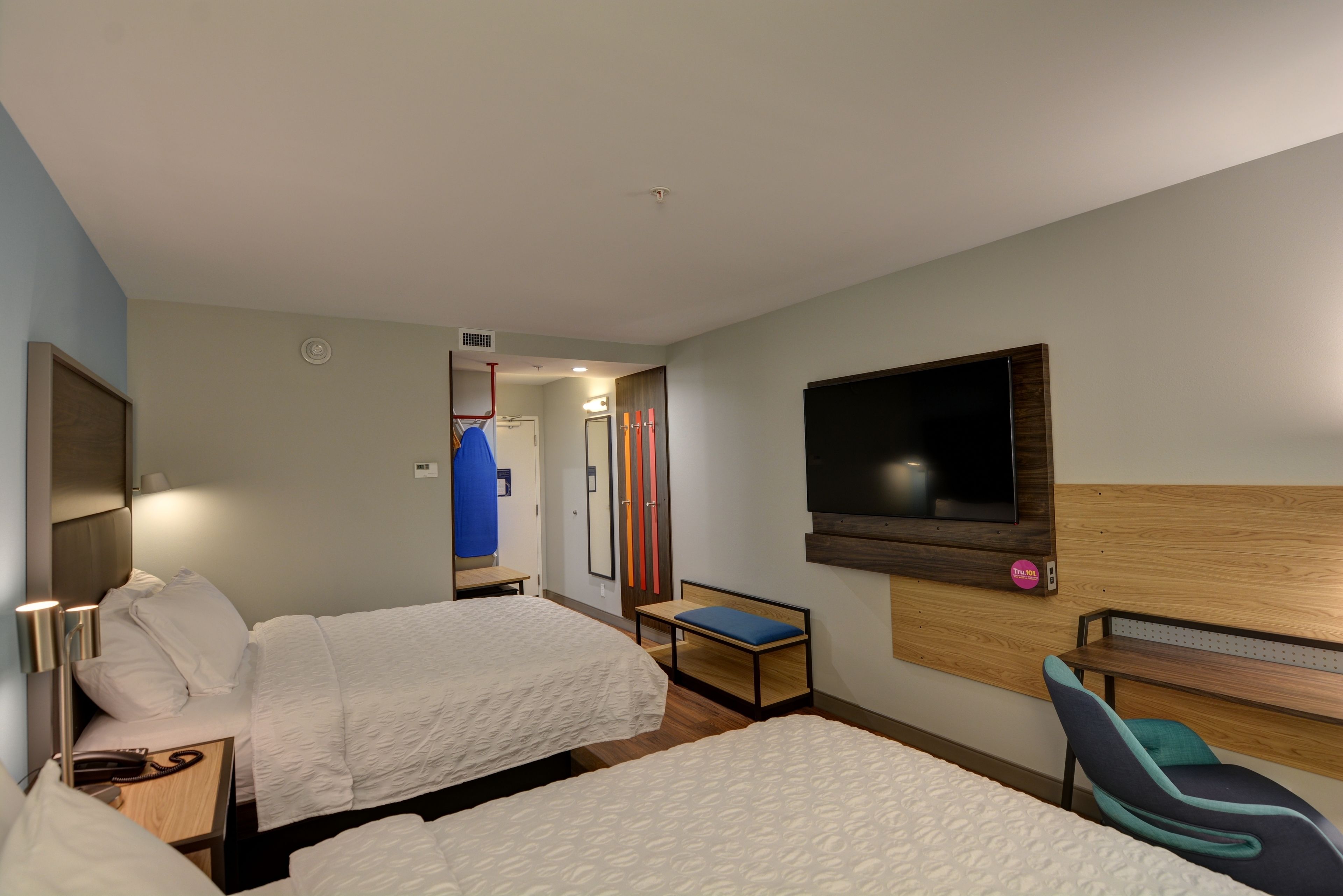 A hotel room with two beds, a TV mounted on the wall, a desk, and a chair.