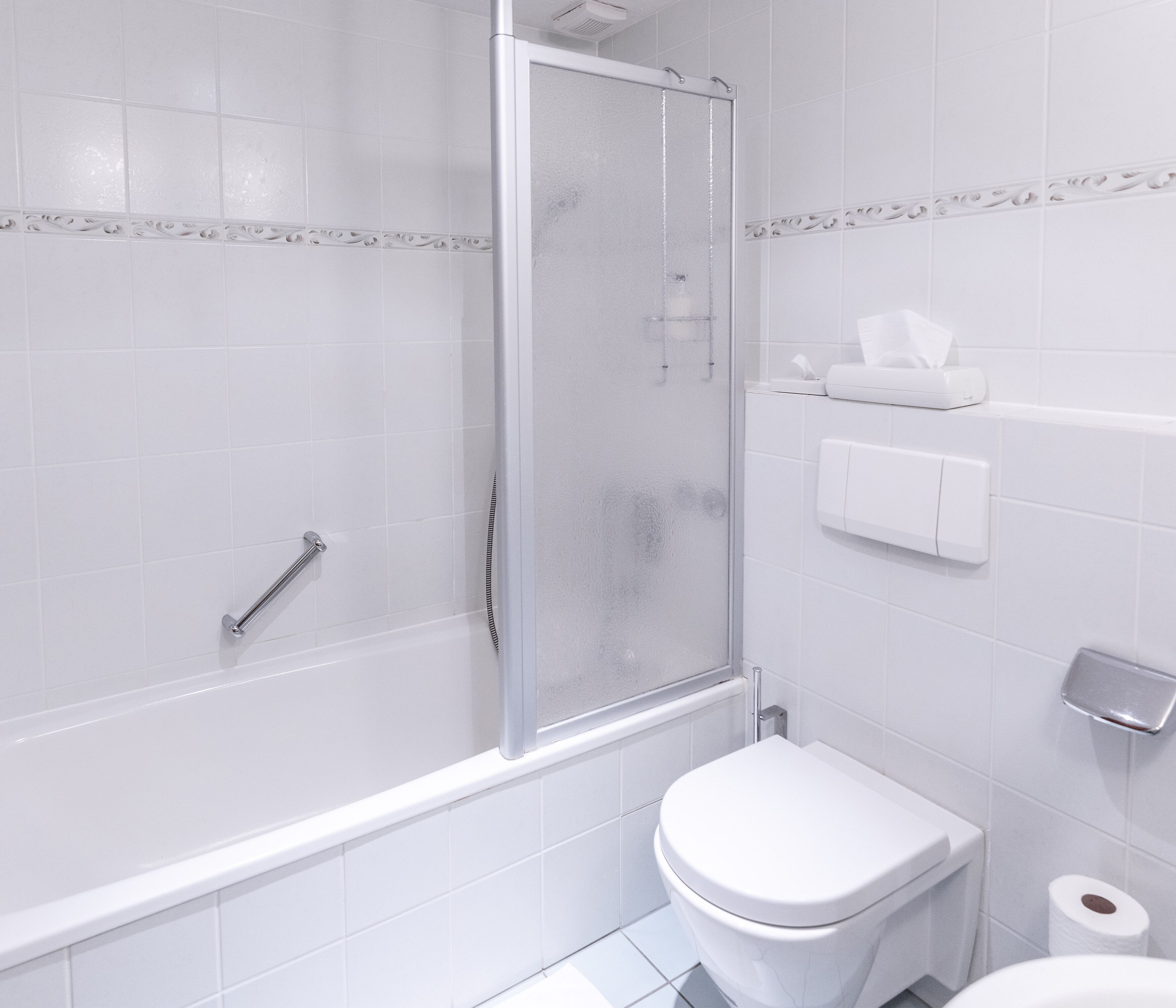 A modern bathroom with a glass-enclosed shower, a toilet, and a paper towel dispenser.
