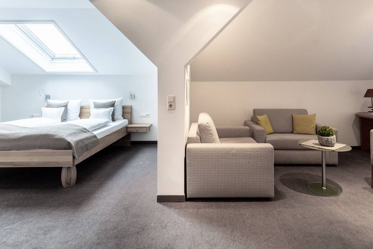 A modern, well-lit room with a bed, a sofa, and a small table.