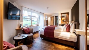 Una habitación de hotel moderna con una cama grande, un televisor montado en la pared, una mesita y una silla.