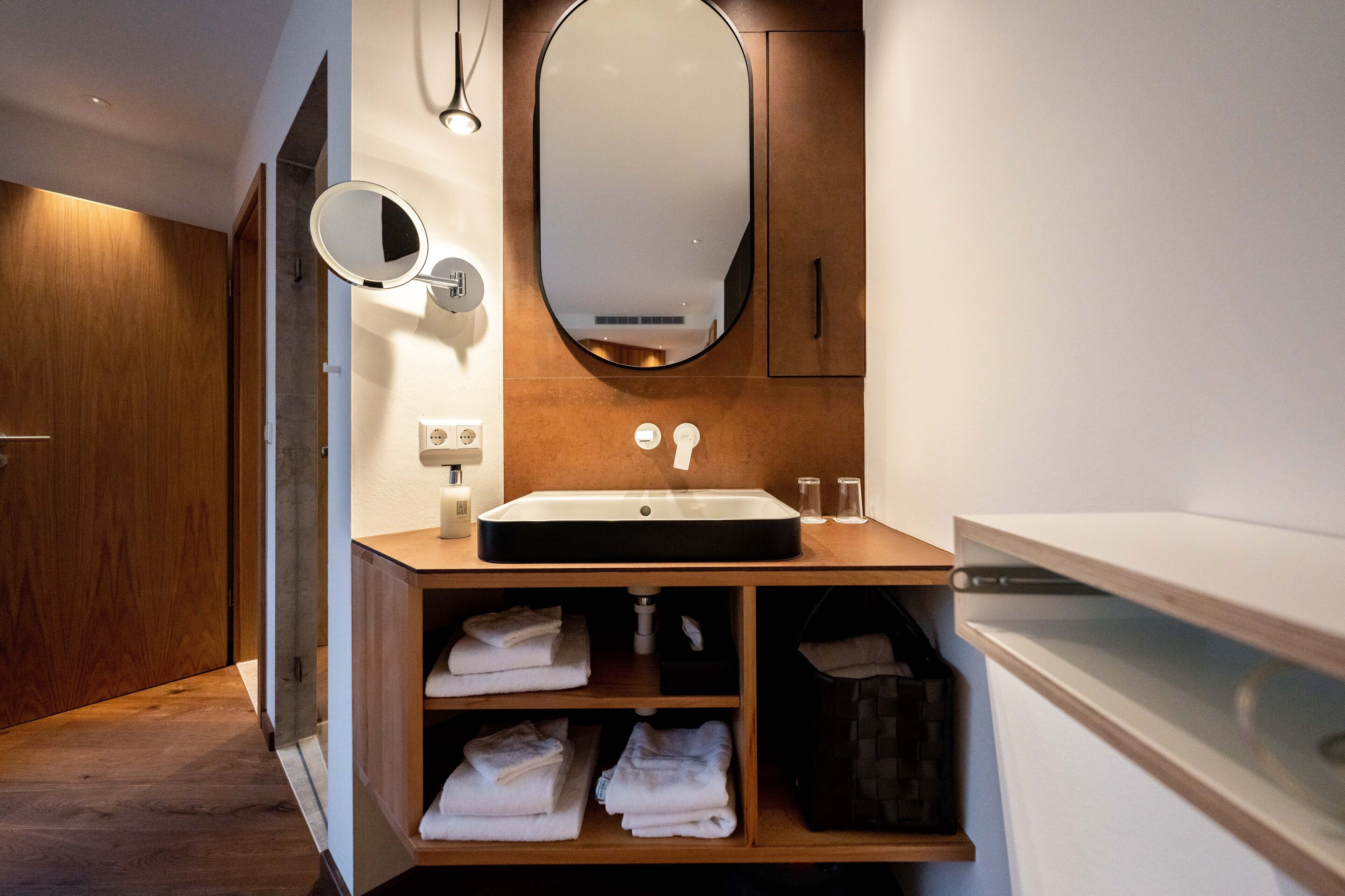 A modern bathroom with a wooden vanity, a large mirror, and a built-in towel rack.