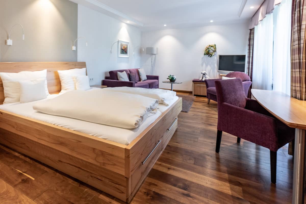 A modern hotel room with a wooden bed, a sofa, a desk, and a TV.
