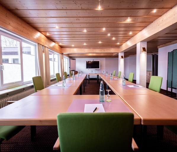 Un salón de conferencias con una larga mesa, sillas verdes y una pantalla de proyector.