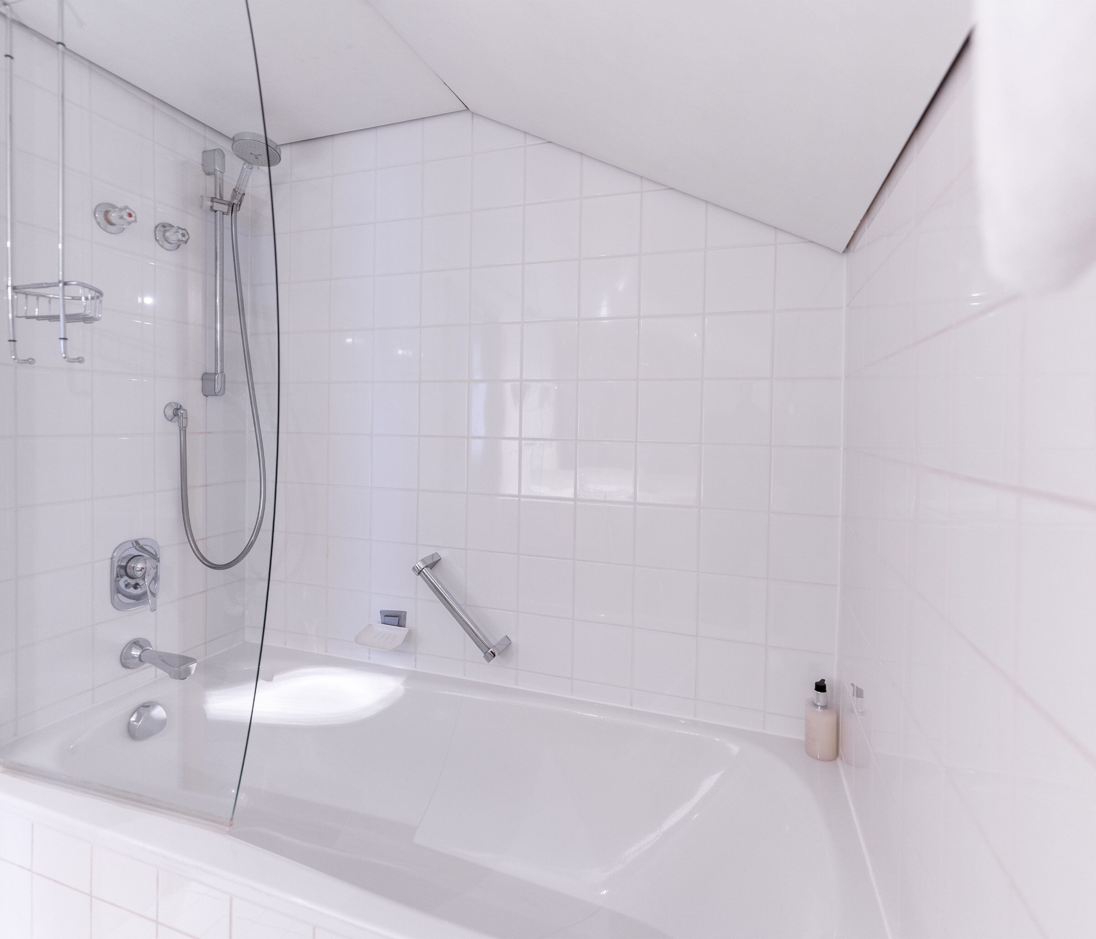Een moderne badkamer met een douche met glazen wand, een badkuip en witte betegelde wanden.