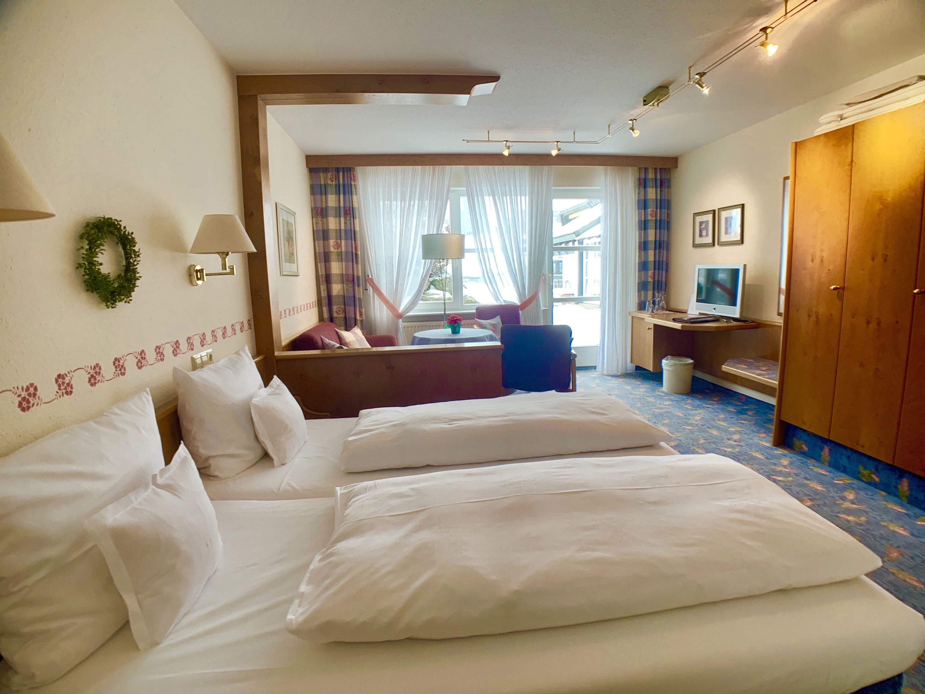 A hotel room with two beds, a desk with a computer, a TV, and a view of the outside.