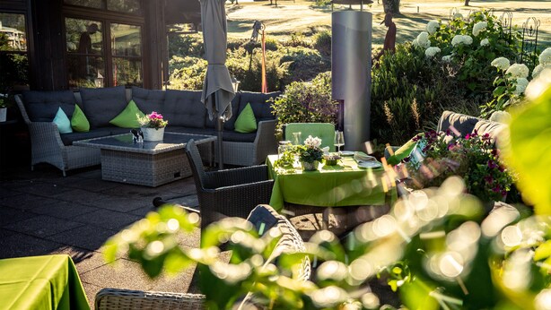 Un área exterior con mobiliario de mimbre, una mesa lista para comer y una vista de un campo de golf al fondo.