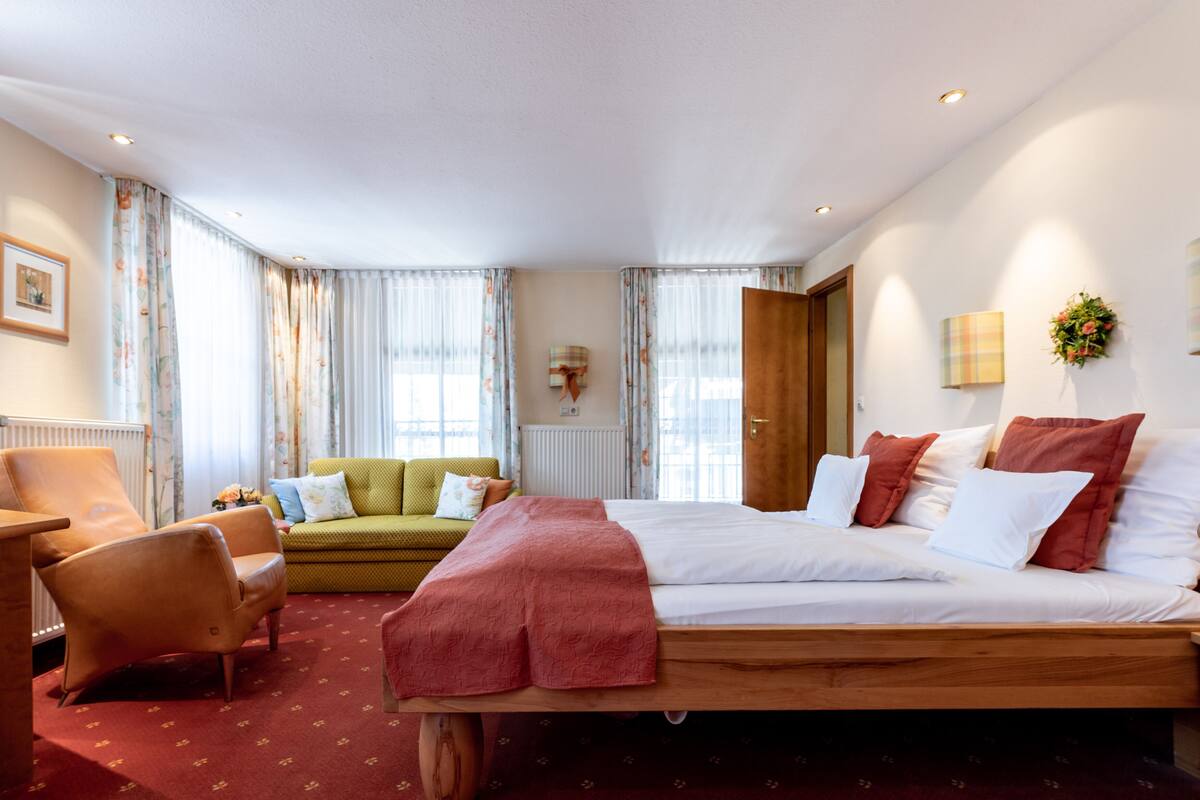 A hotel room with a large bed, a sofa, a chair, and a window with curtains.