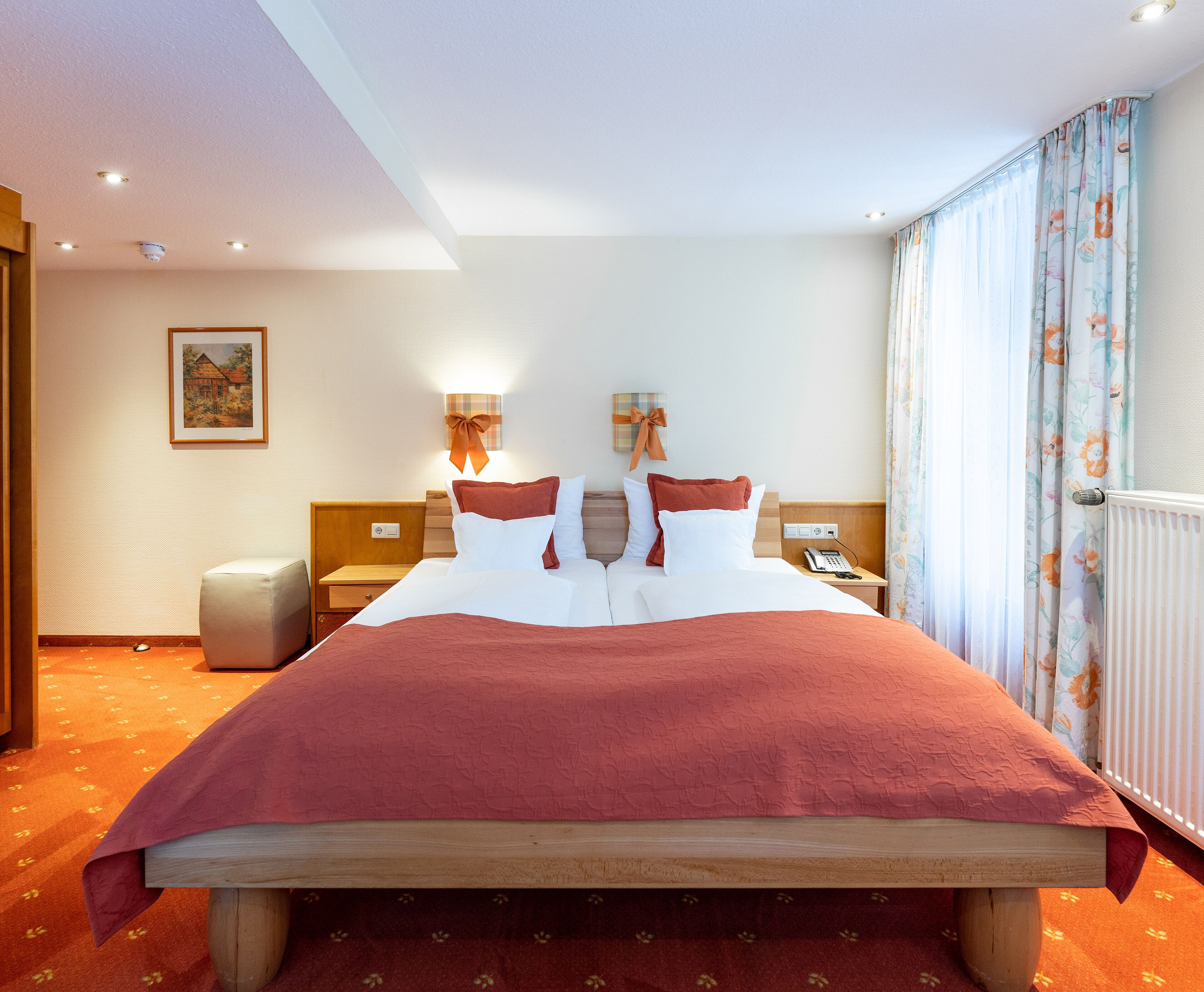 A hotel room with a large bed, a bedside table with a lamp, a telephone, and a radiator.