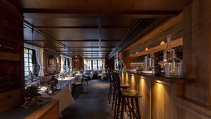 Un restaurante con interiores de madera, mesas dispuestas para comer y una zona de bar con taburetes.