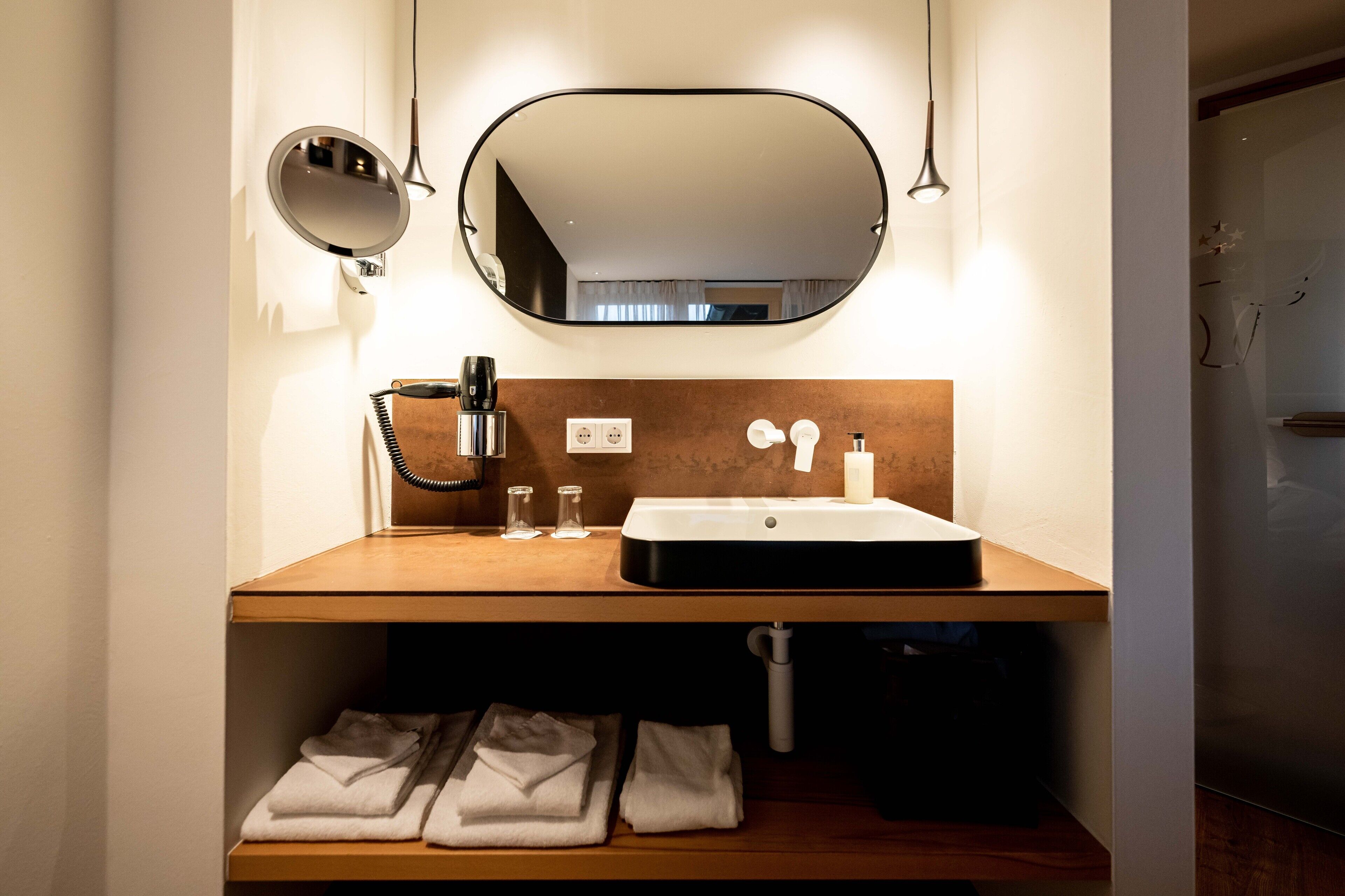 Een moderne badkamer met een houten wastafelmeubel, een ronde spiegel, een wastafel en een handdoekhouder.