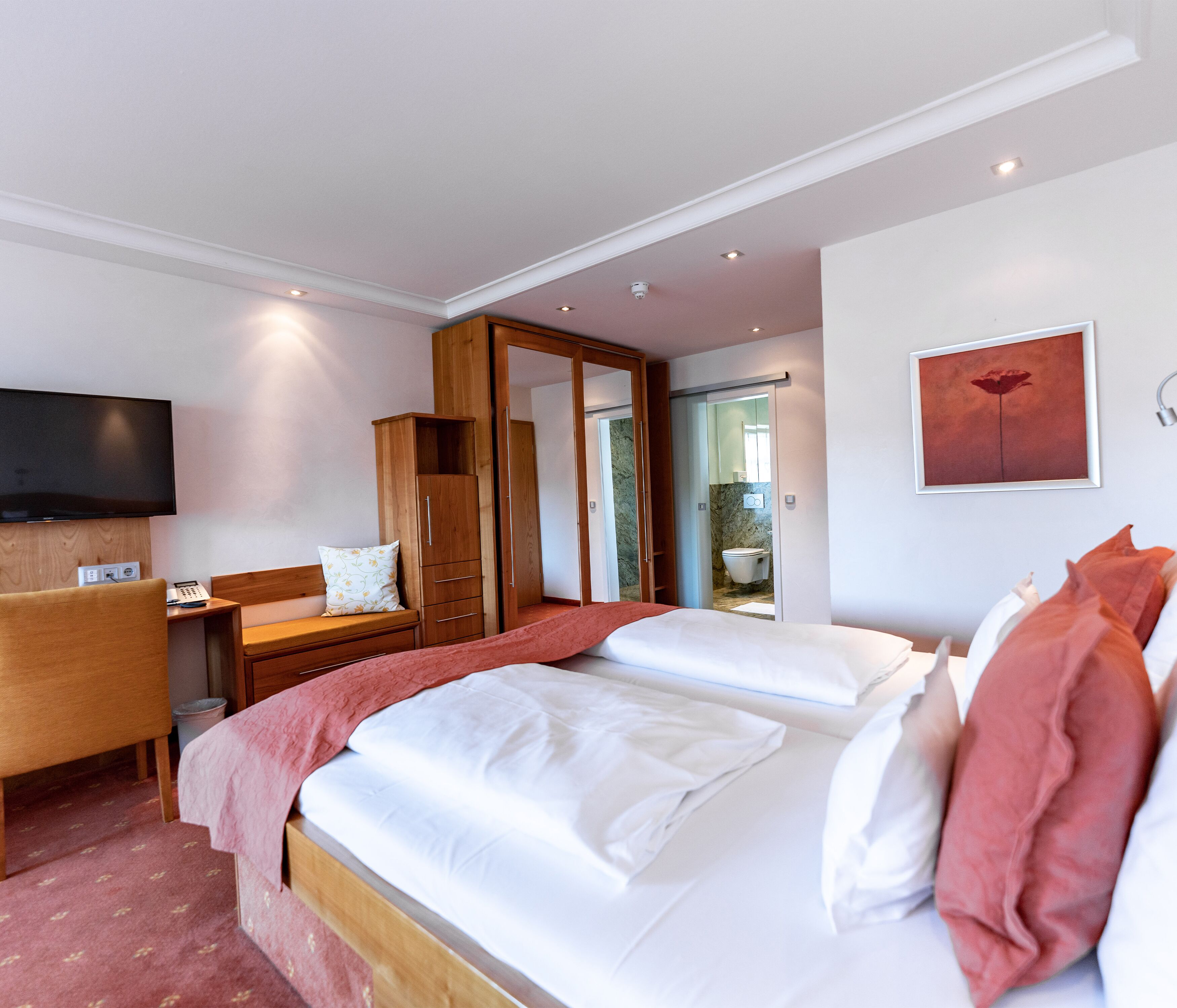A hotel room with a bed, a desk, a chair, a TV, and a wardrobe.