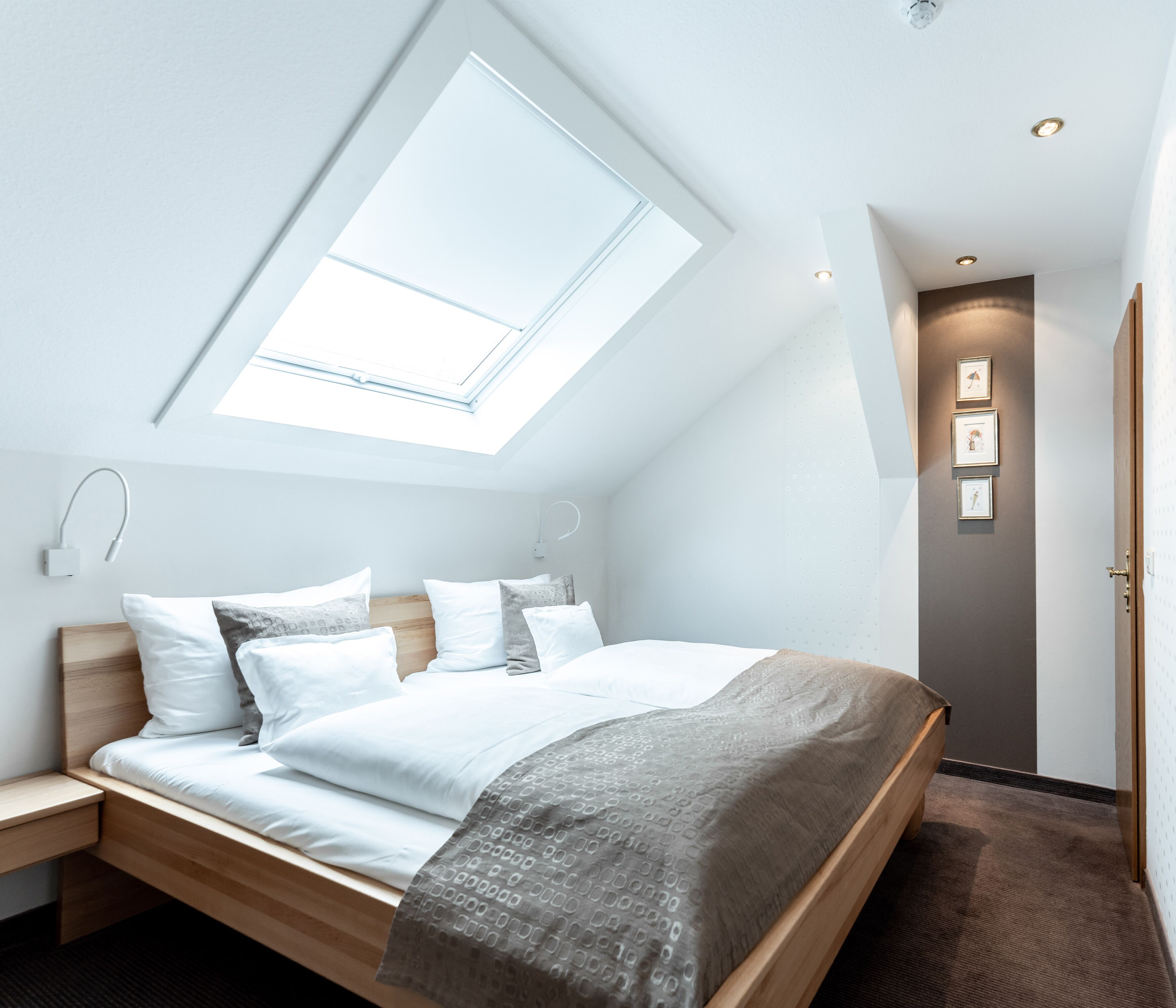 A modern bedroom with a skylight, a bed with white bedding, a wooden headboard, and a bedside table.