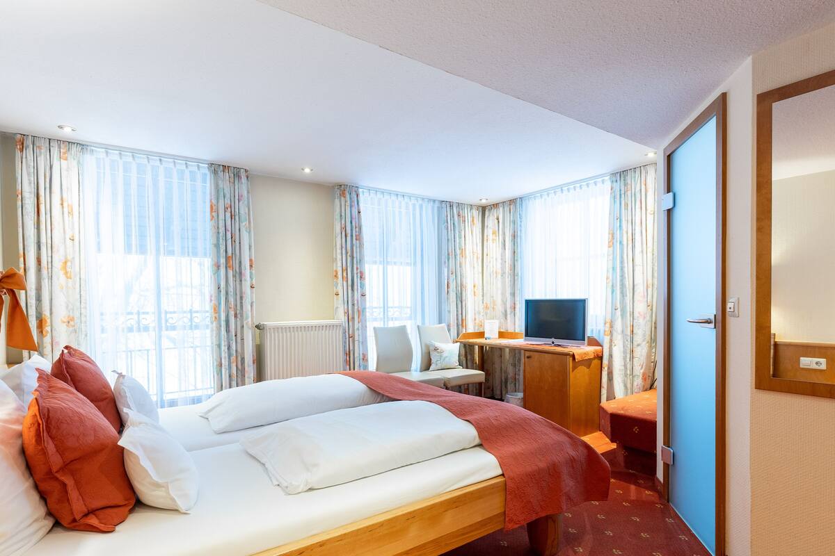 A hotel room with a bed, a desk with a computer, a chair, and a TV.