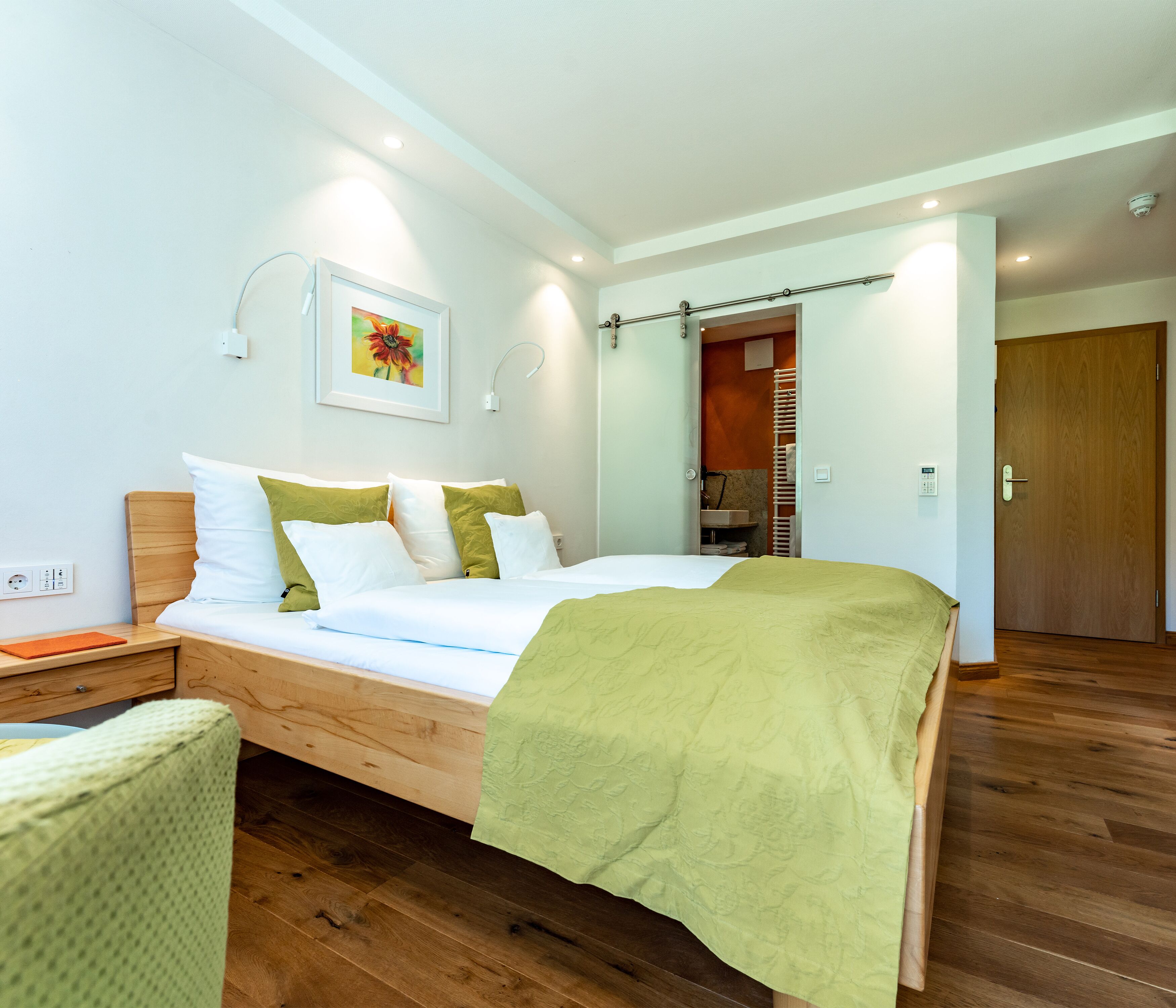 Ein modernes Schlafzimmer mit einem Holzbett, einem Nachttisch, einer Wandleuchte, einem gerahmten Bild und einer Holztür.