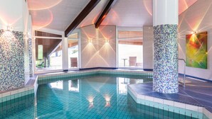 Una piscina interior con agua azul cristalina, paredes con azulejos y un diseño arquitectónico moderno con pilares grandes y techo inclinado.