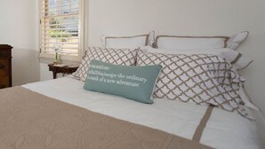 Una cama bien tendida con almohadones estampados y un cojín decorativo con texto.