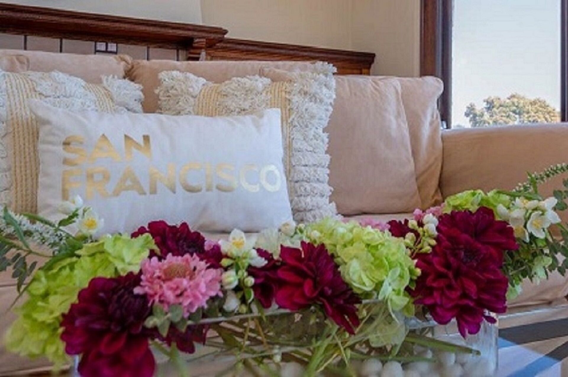 Un divano con un cuscino con la scritta "SAN FRANCISCO" e un composizione floreale di fronte.