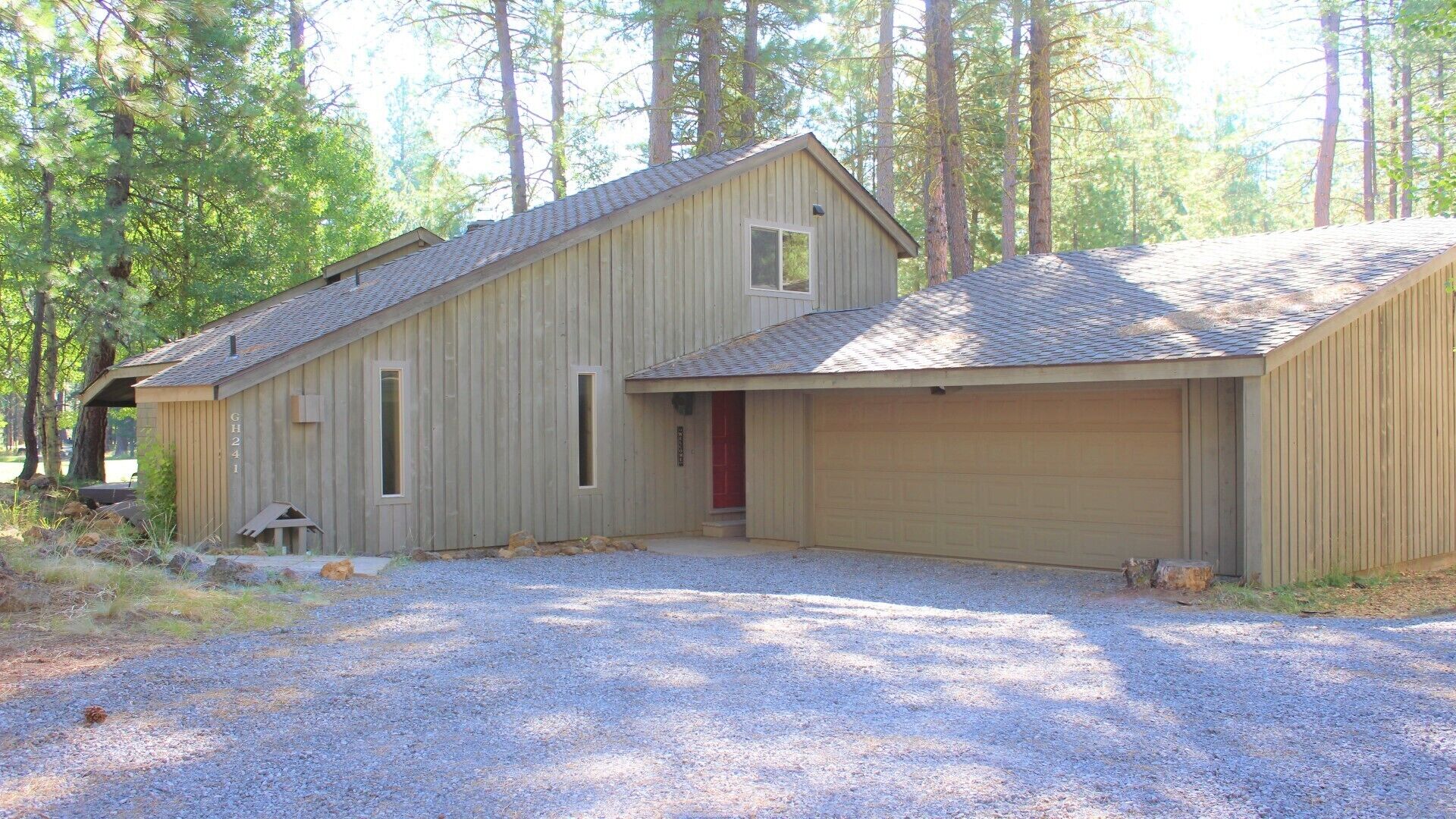 A single-story wooden building with a garage, surrounded by trees.