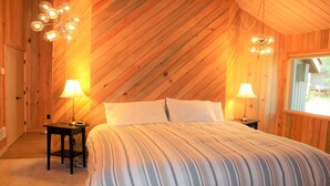 Une chambre avec un plafond en bois incliné, deux lampes de chevet, un lit avec une literie à rayures et une fenêtre sur le côté droit.
