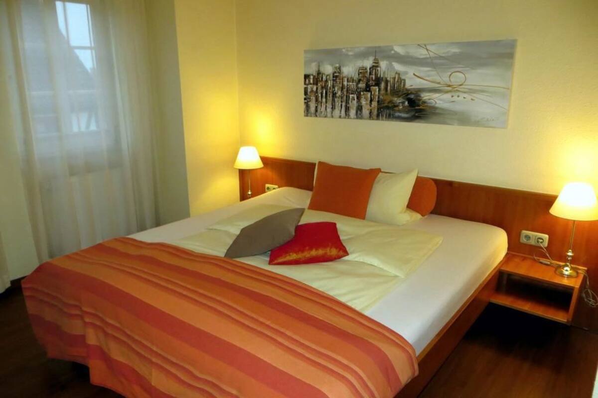 Een hotelkamer met een groot bed, twee bedlampjes, een schilderij aan de muur en een raam met gordijnen.