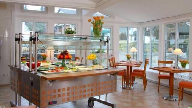 Un área de bufé con un expositor de vidrio, varias mesas de comedor y sillas.