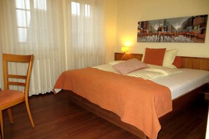 A hotel room with a bed, a chair, a painting on the wall, and a window with curtains.
