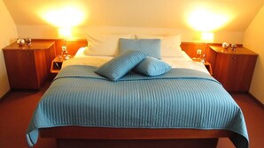 Una cama bien hecha con cubrecama y almohadas azules, flanqueada por dos mesitas de noche con lámparas, en una habitación con techo inclinado.