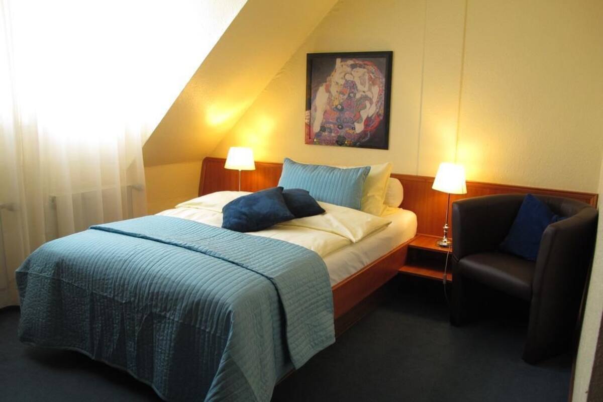 Een hotelkamer met een bed, twee bedlampen, een stoel en een schilderij aan de muur.
