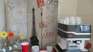 Una mesa con una cafetera, tazas blancas, una taza roja y un fondo decorativo de la Torre Eiffel.