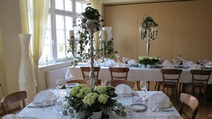 Un comedor con mesas dispuestas para un evento formal, con manteles blancos, cristalería y centros de mesa florales.
