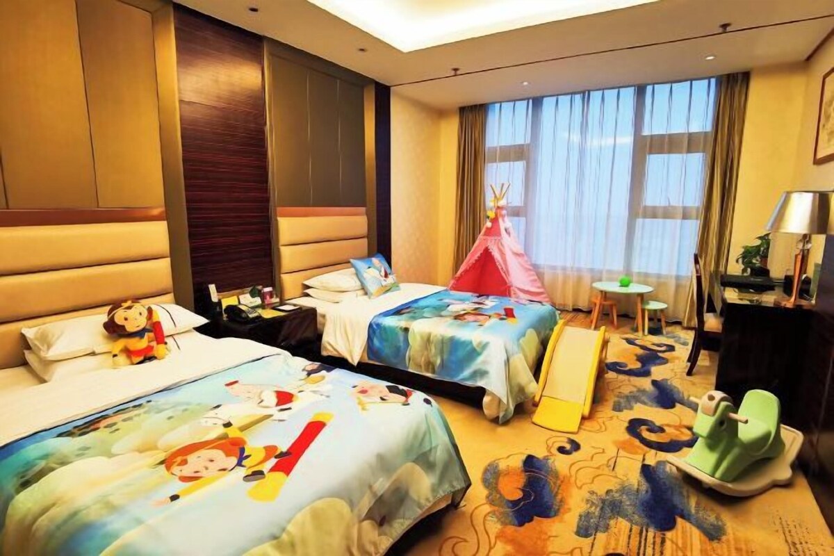 A hotel room with two beds, a small table, a chair, a tent, and a window with curtains.