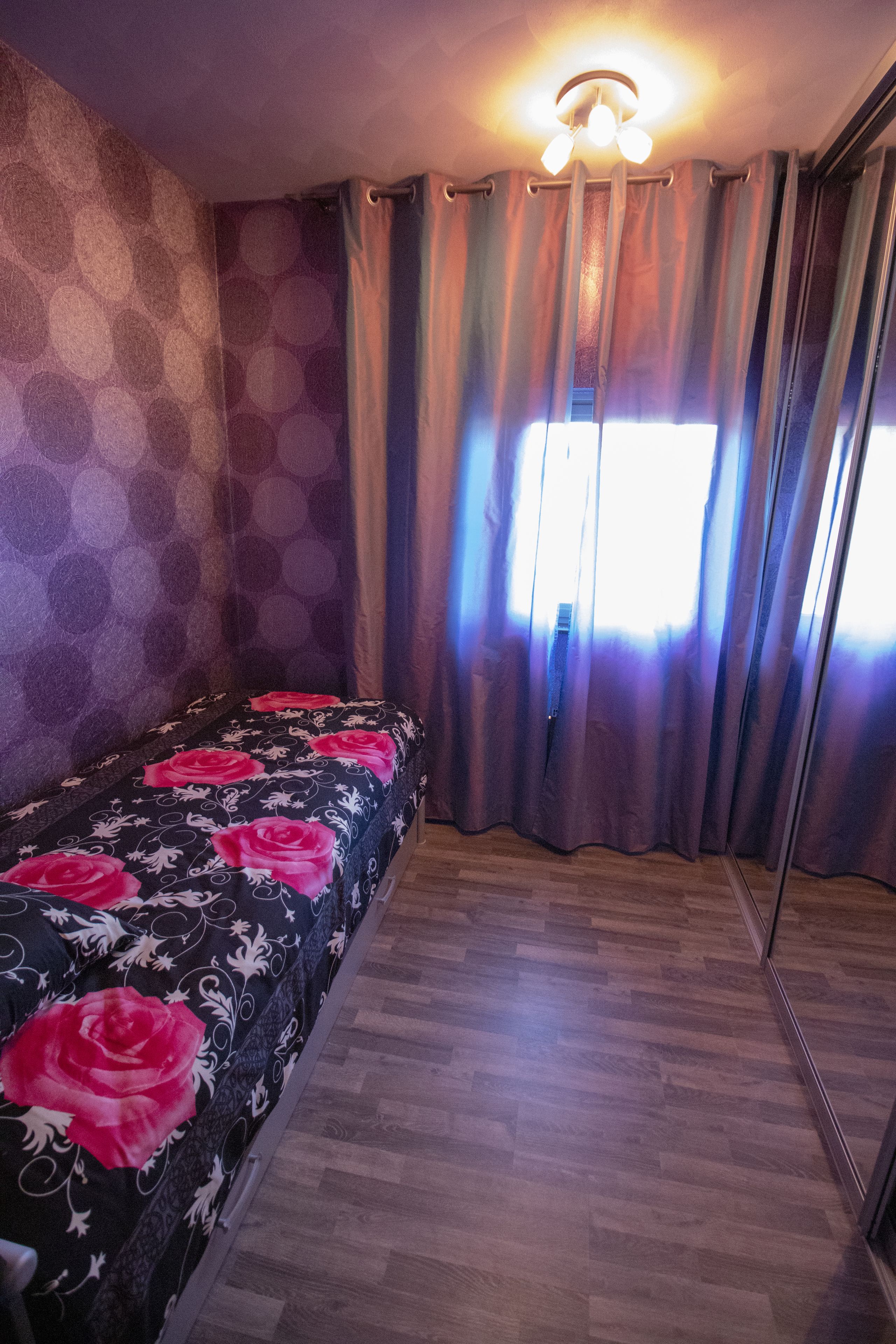 A room with a bed, a ceiling light, and a window with curtains.