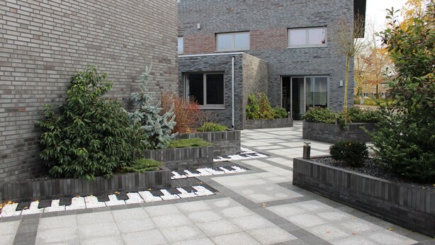 Un edificio moderno con fachada de ladrillo, zonas de estar exteriores con jardineras y un patio empedrado.