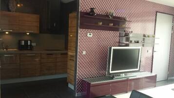 A modern kitchen with dark wood cabinets, a built-in oven, and a flat-screen TV mounted on a textured wall.