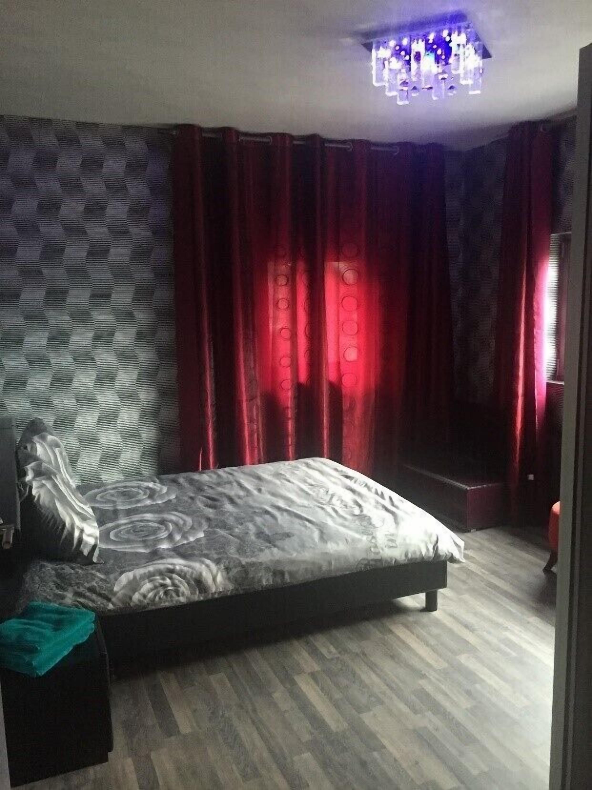 Un dormitorio con cama, pared con diseño de piedra, cortinas rojas y lámpara de techo.