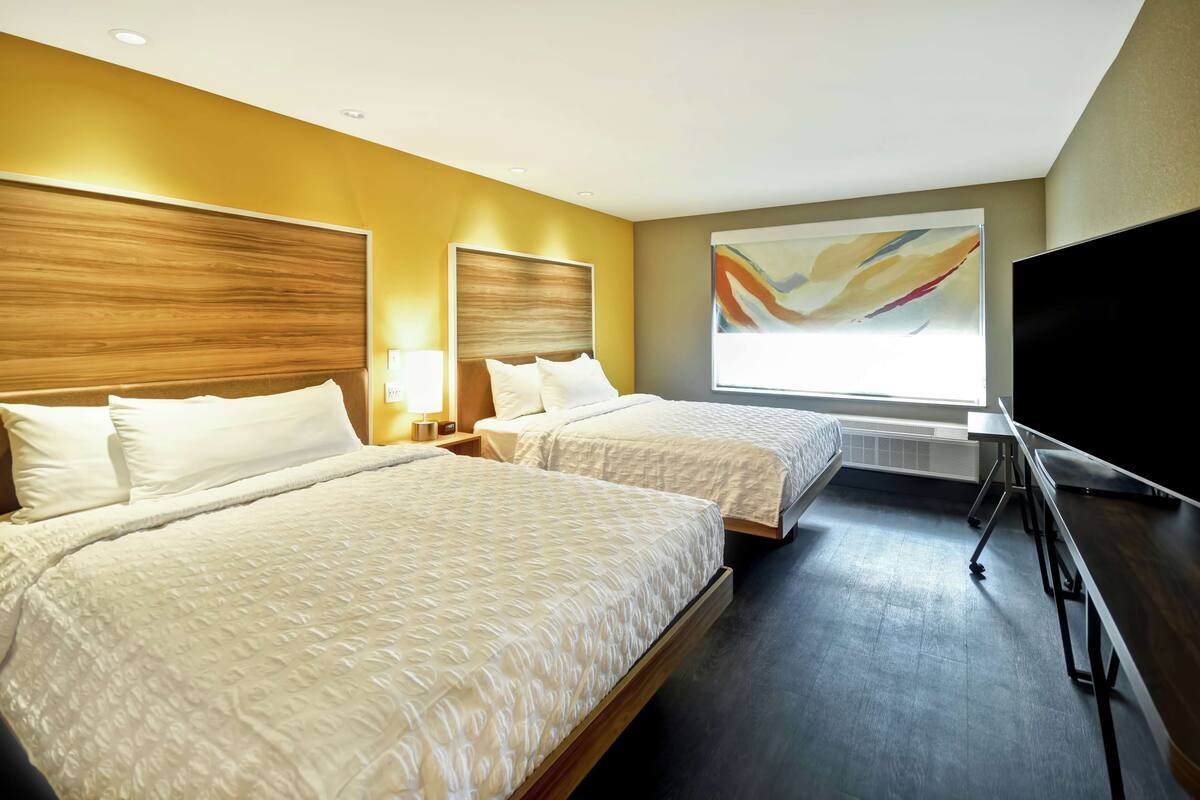 Une chambre d’hôtel avec deux lits, un téléviseur à écran plat et un grand tableau abstrait accroché au mur.