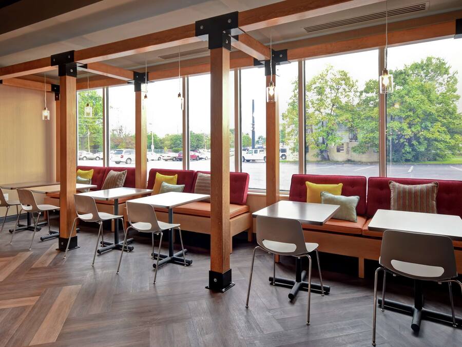 Un café moderno con vigas de madera, ventanas amplias y una variedad de opciones de asientos, incluyendo mesas y bancos.