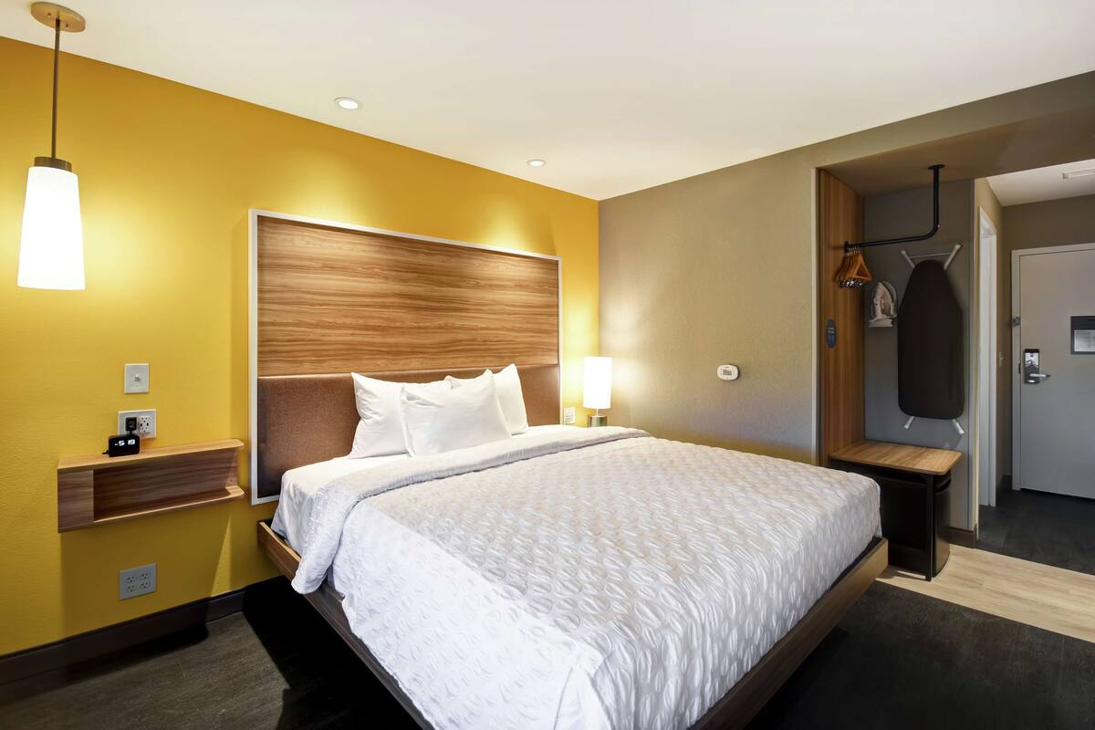 Une chambre d’hôtel avec un grand lit, une tête de lit en bois, une table de chevet avec une lampe et une armoire.